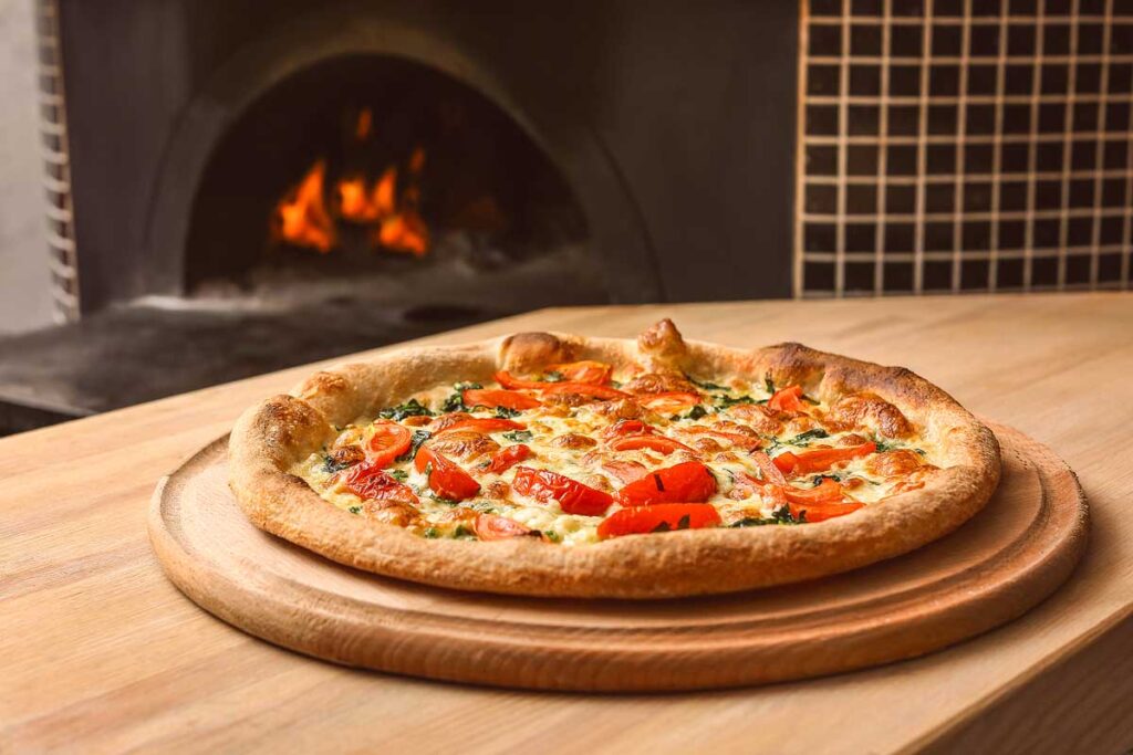 Tasty pizza on table against stove in kitchen.