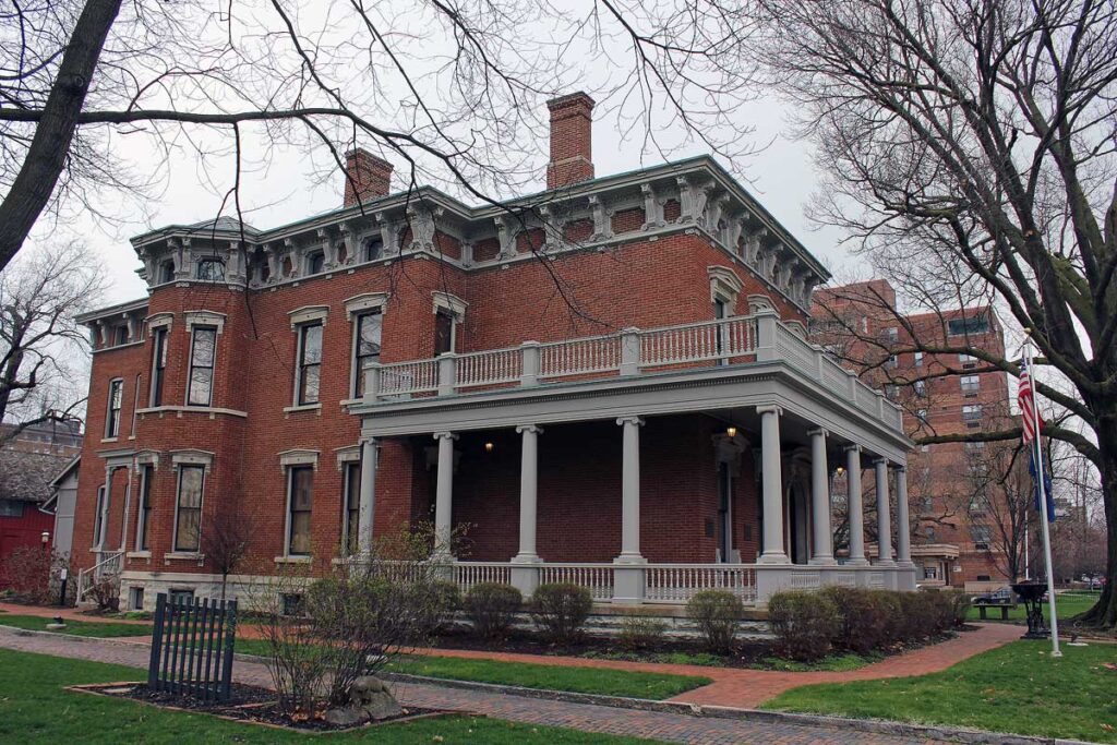 Stately home of 23rd USA President Benjamin Harrison welcomes visitors. Expansive porch with columns and balcony, plus large corbels and chimneys.