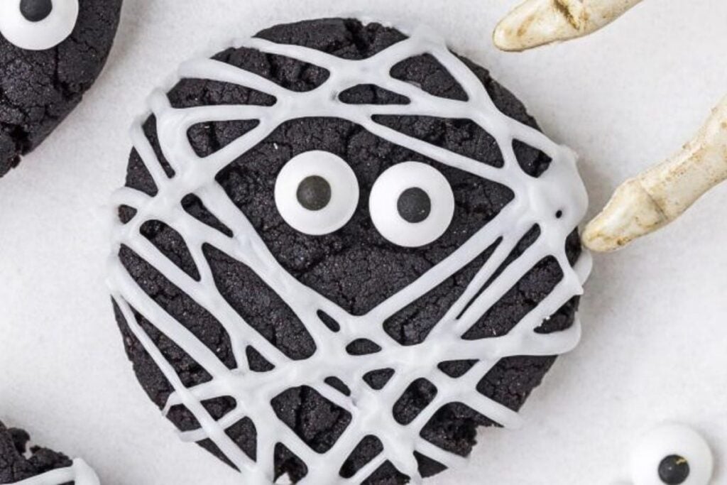 Chocolate cookies decorated to look like mummies with frosting and eyes.