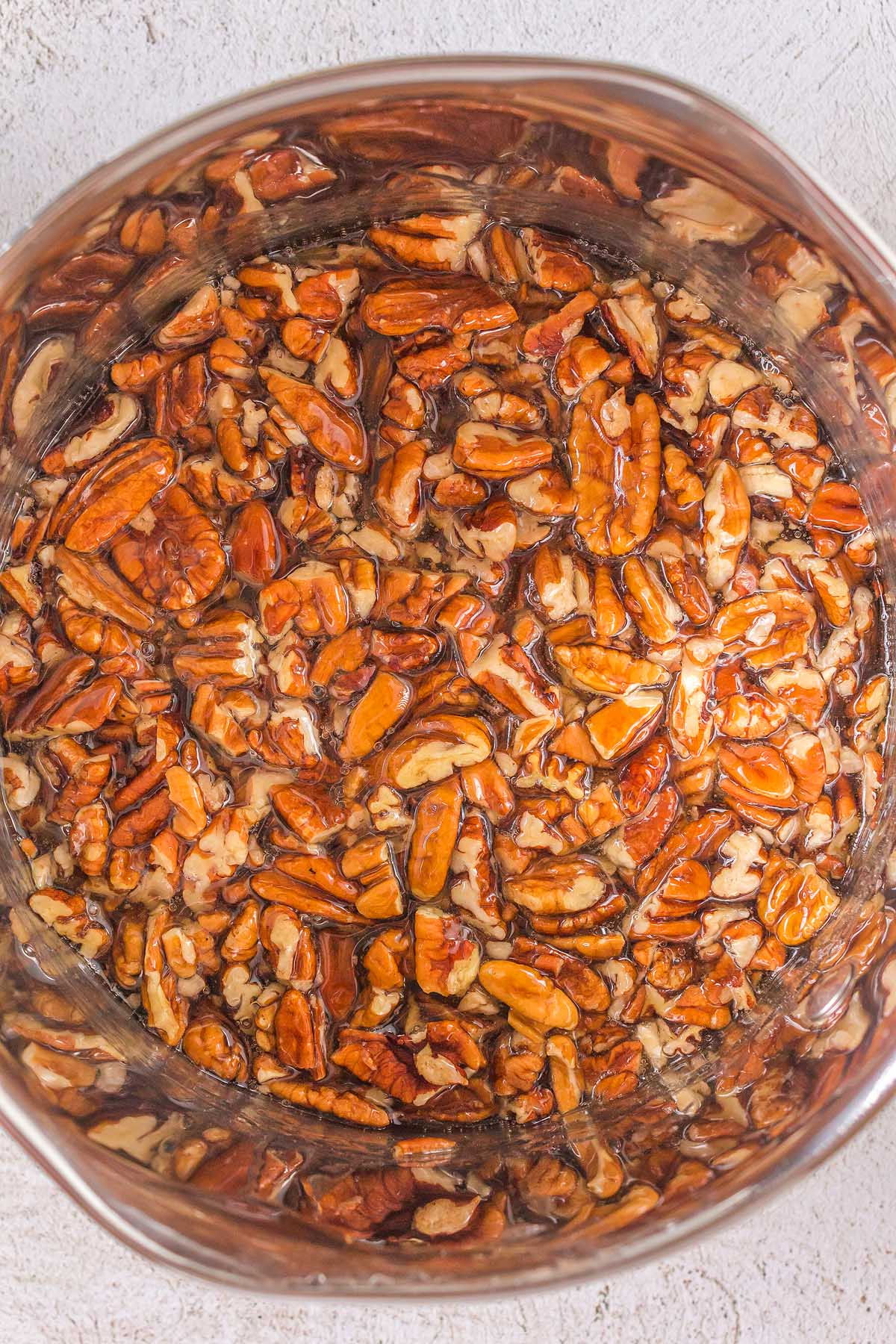 Crunchy pecans in a bowl on a white surface.
