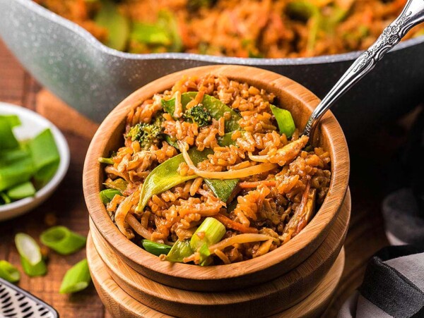 A stack of wooden bowls with homemade PF Chang's Fried Rice in it. The copycat recipe was made in a wok which is in the background.