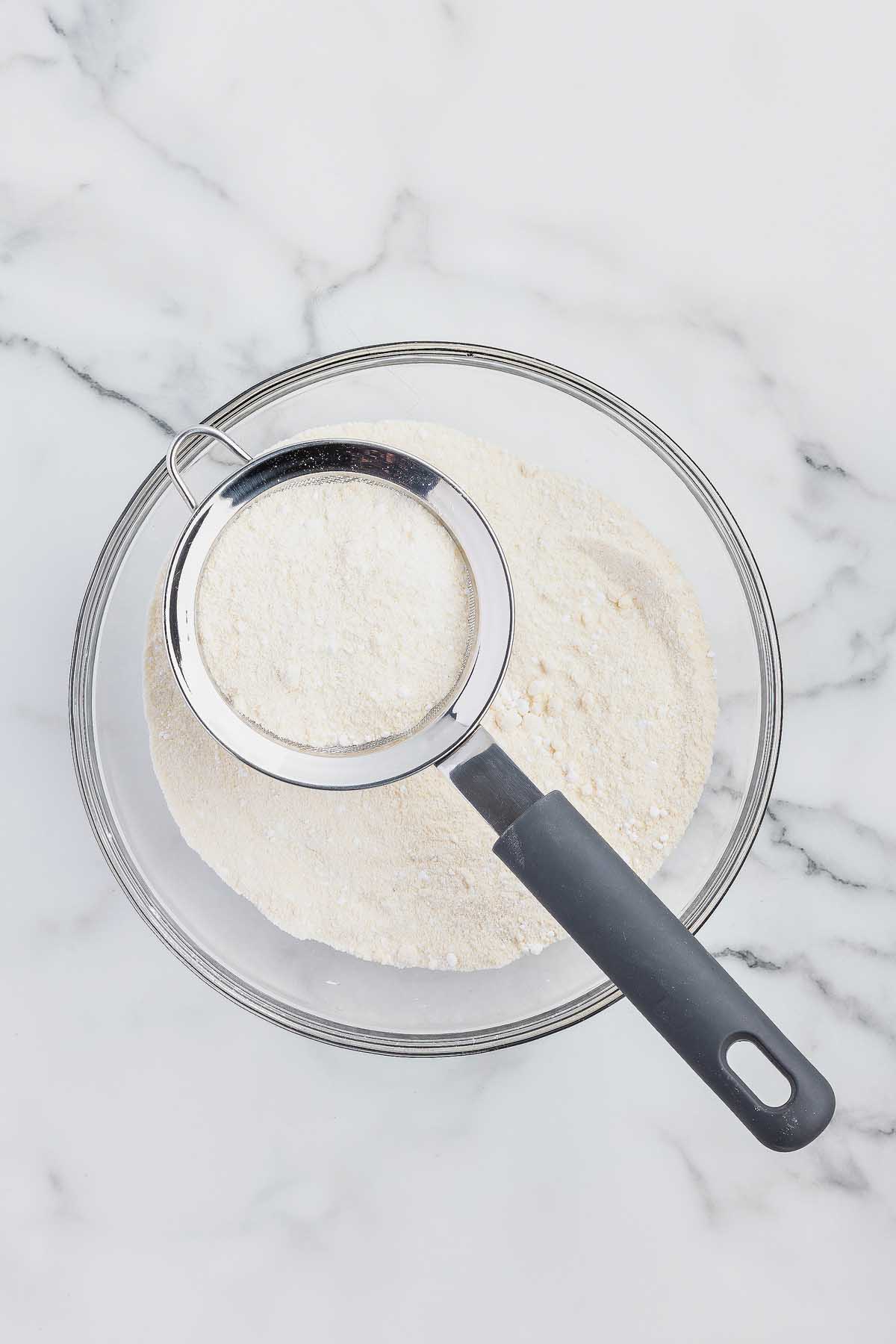 A scoop of flour in a bowl on a countertop.