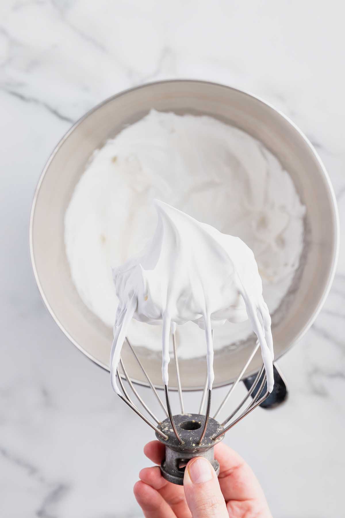 A hand holding a whisk with whipped cream in it, creating delectable cookies.