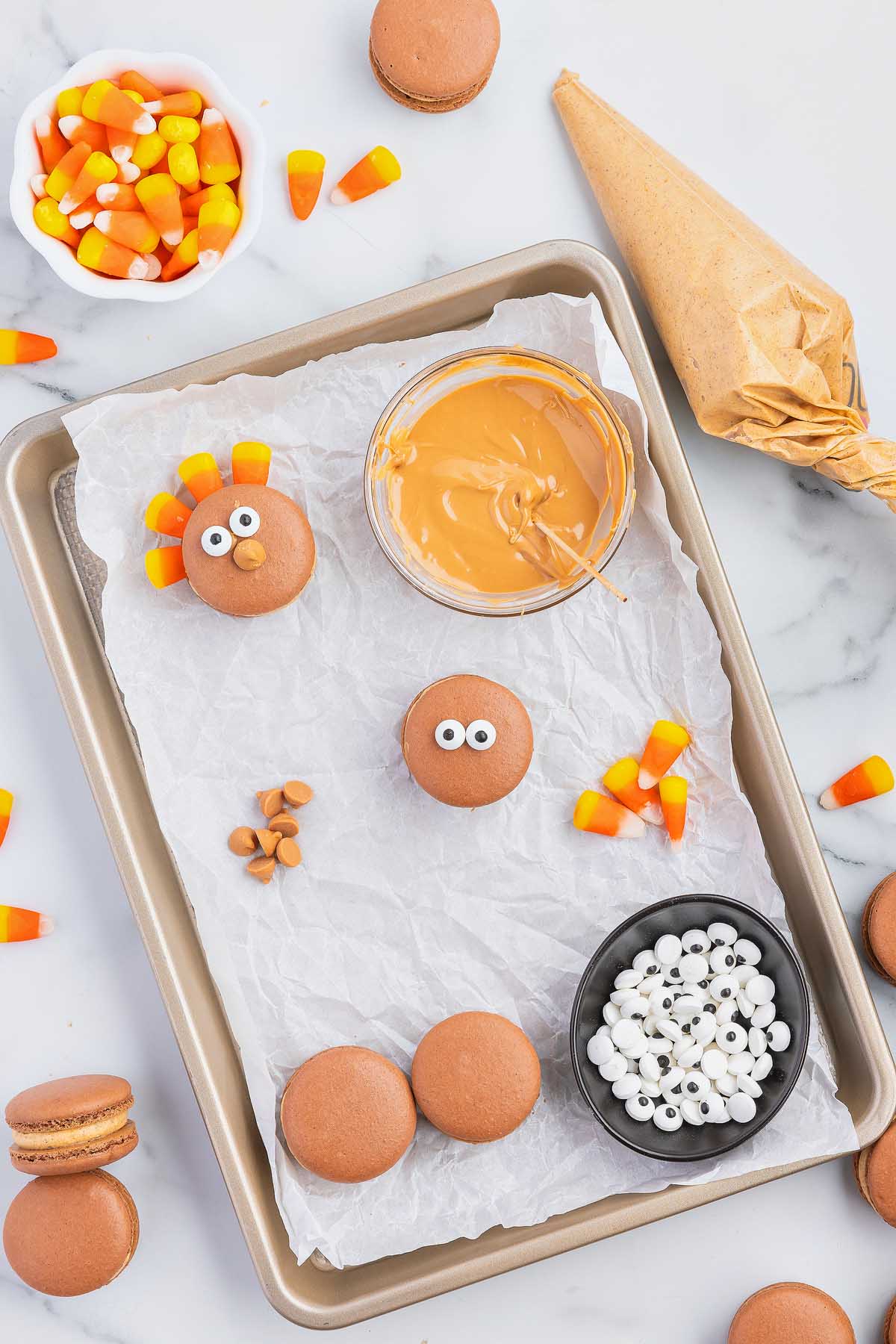 Thanksgiving macarons on a baking sheet with candy corn and candy eyes.