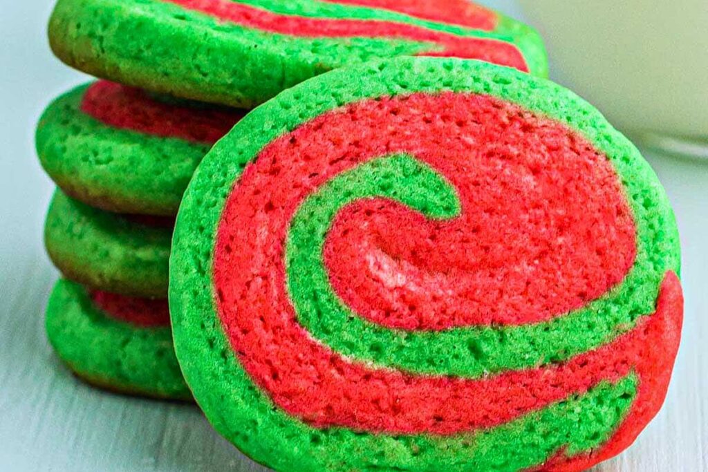Green and red Christmas pinwheel cookies stacked on wood backdrop.