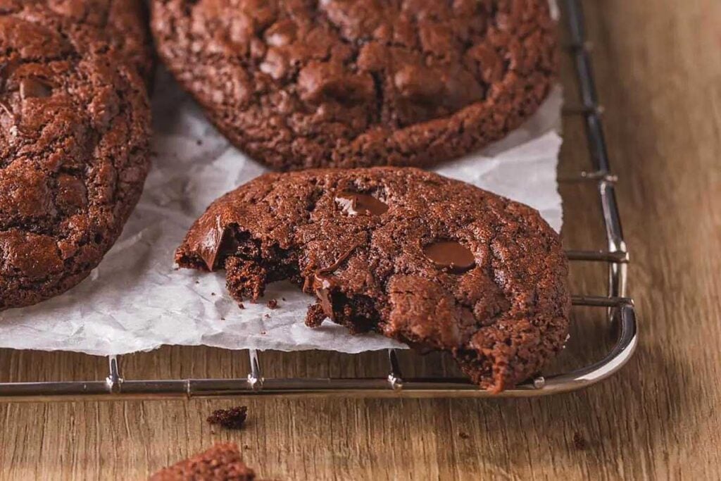 Gluten-free chocolate cookies on a cooling rack with a bite taken out.