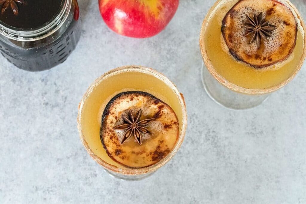 Coupe glases with spiced apple cocktails and apple slices inside.