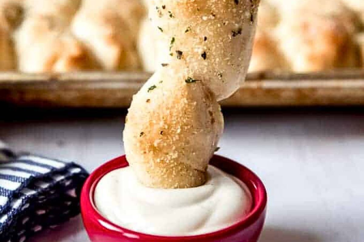 A hand dipping a bread stick into creamy sauce.