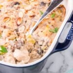 Creamy mushroom gruyere Chicken and Rice Casserole in a blue baking dish, garnished with fresh herbs and sliced almonds.