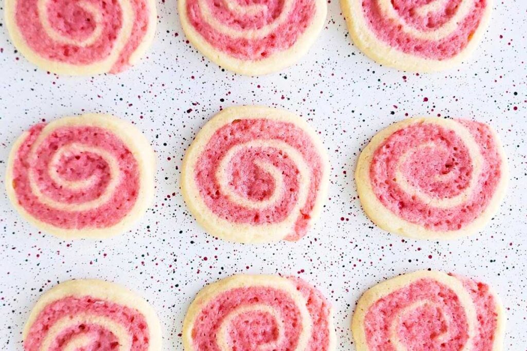 Delicate pink and white peppermint pinwheel cookies carefully arrange on speckled backdrop.