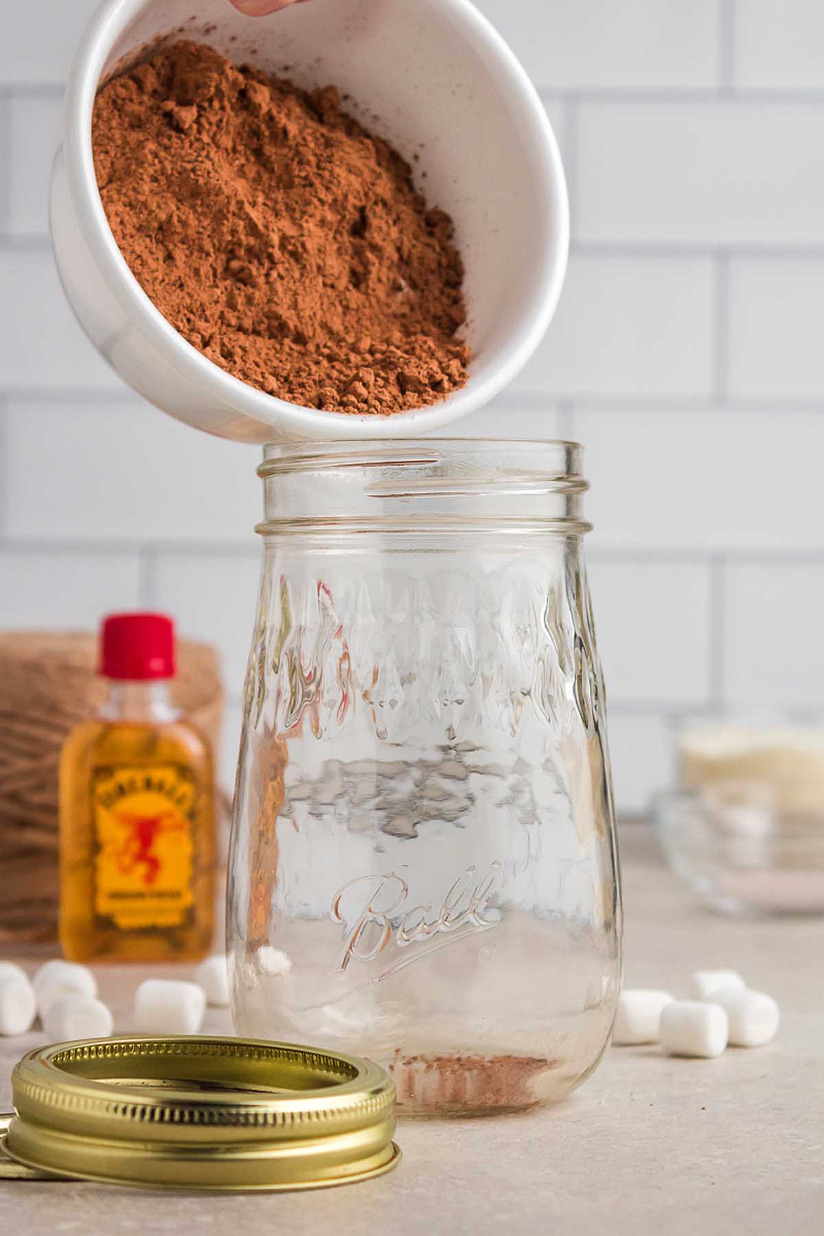 A person pouring cocoa powder into a mason jar, creating a delightful handmade Christmas gift.