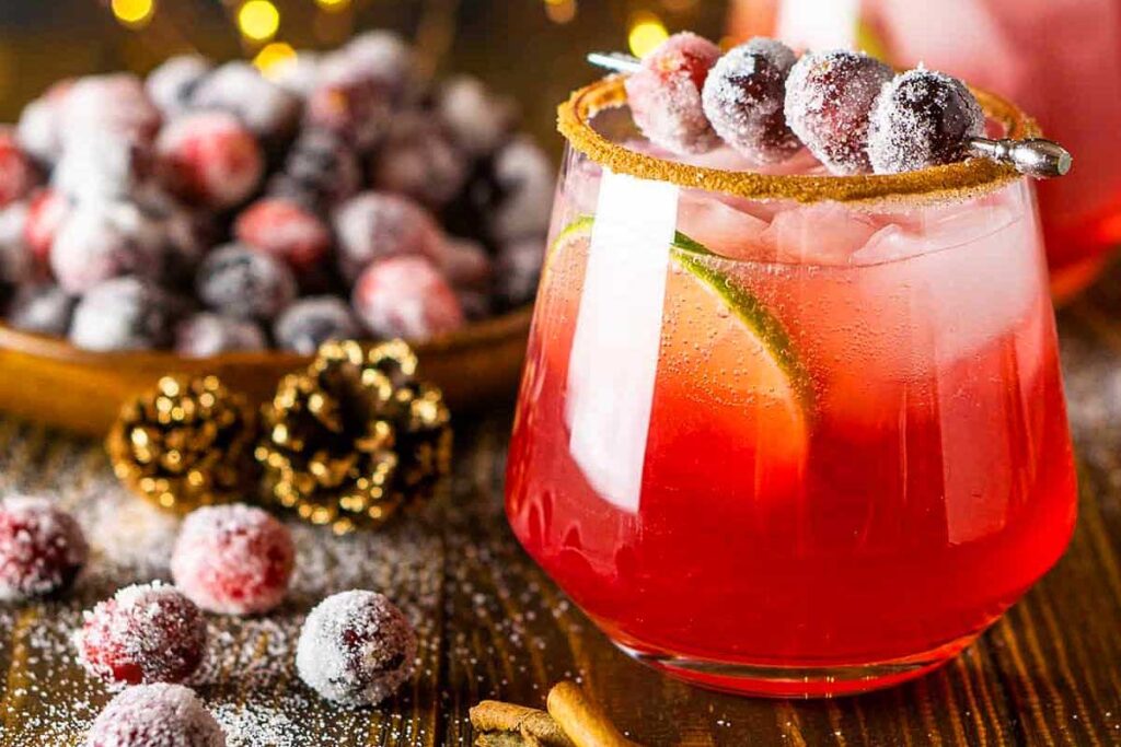 A festive red cocktail with lime slices and sugared cranberries, garnished with a sugar rim—perfect for raising a toast at your Friendsgiving celebration.