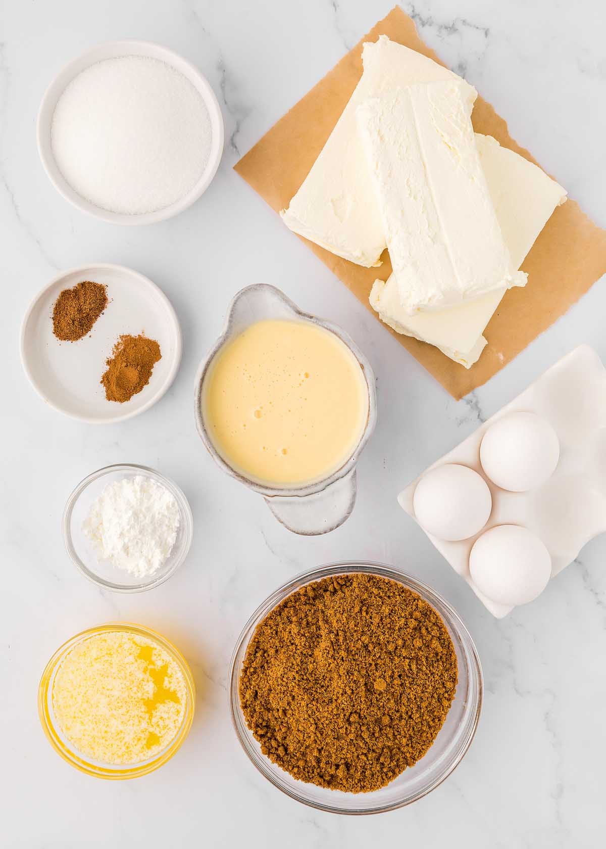 The ingredients for an eggnog cheesecake are shown on a marble table.