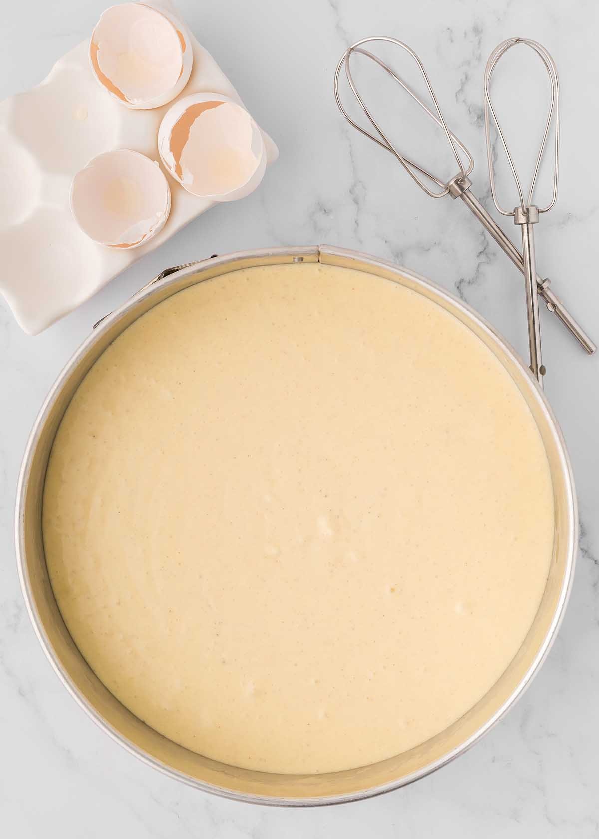 A metal pan with eggs and whisks next to it, ideal for preparing an eggnog cheesecake recipe.