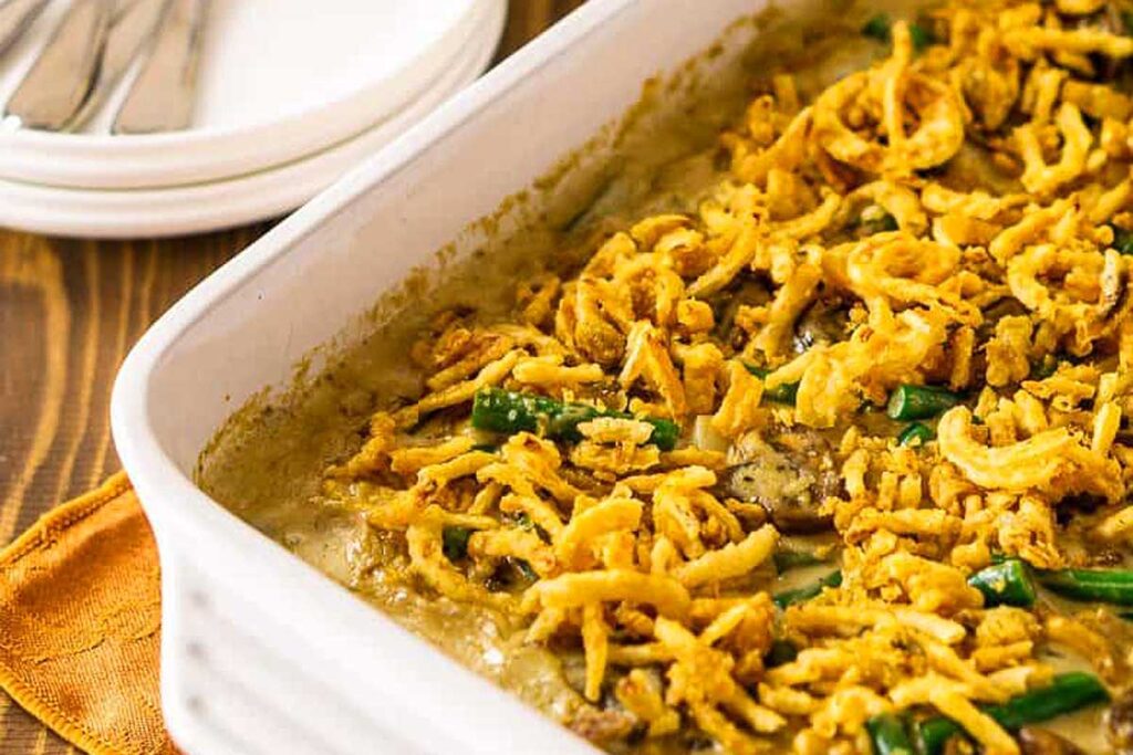 A close-up of green bean casserole topped with crispy fried onions in a white baking dish, perfect for sharing at Friendsgiving.