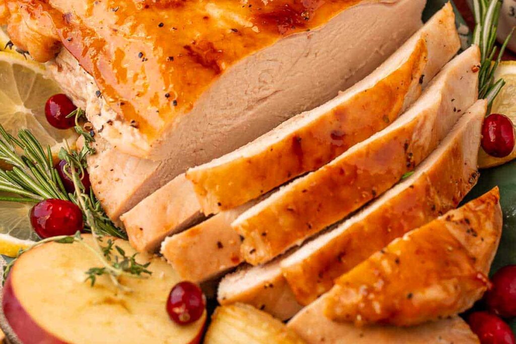Sliced roasted turkey breast with golden skin, garnished with apple slices, cranberries, and rosemary—perfect for a festive Friendsgiving gathering.