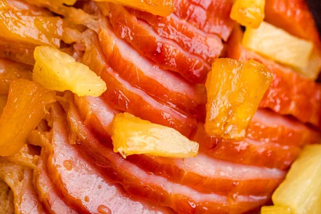 Close-up of glazed, sliced ham topped with chunks of pineapple—a perfect centerpiece for your Friendsgiving feast.