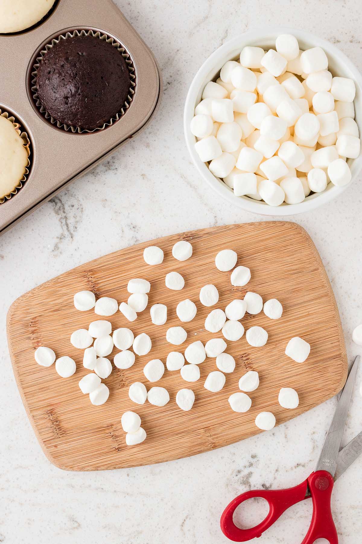 Christmas-themed marshmallows on a cutting board next to a muffin tin.