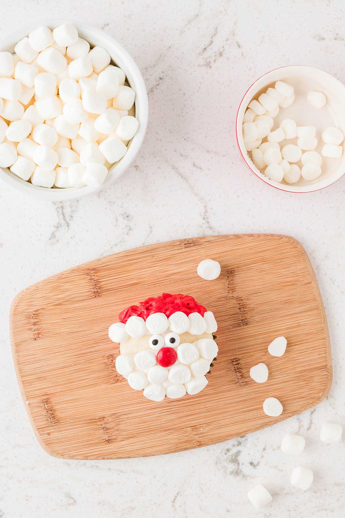 Santa Claus marshmallows on a cutting board with santa-themed treats.