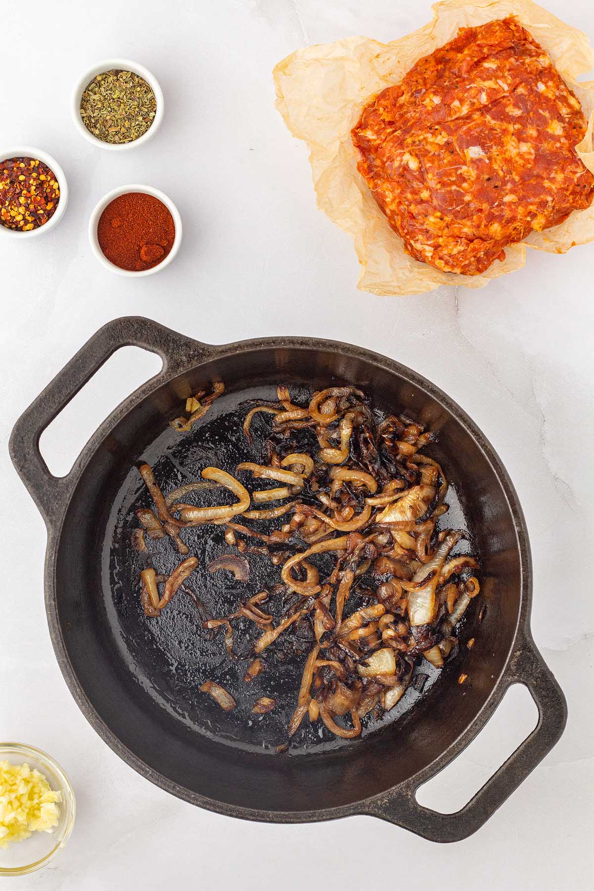 An Italian sausage frying pan with onions and spices next to it.