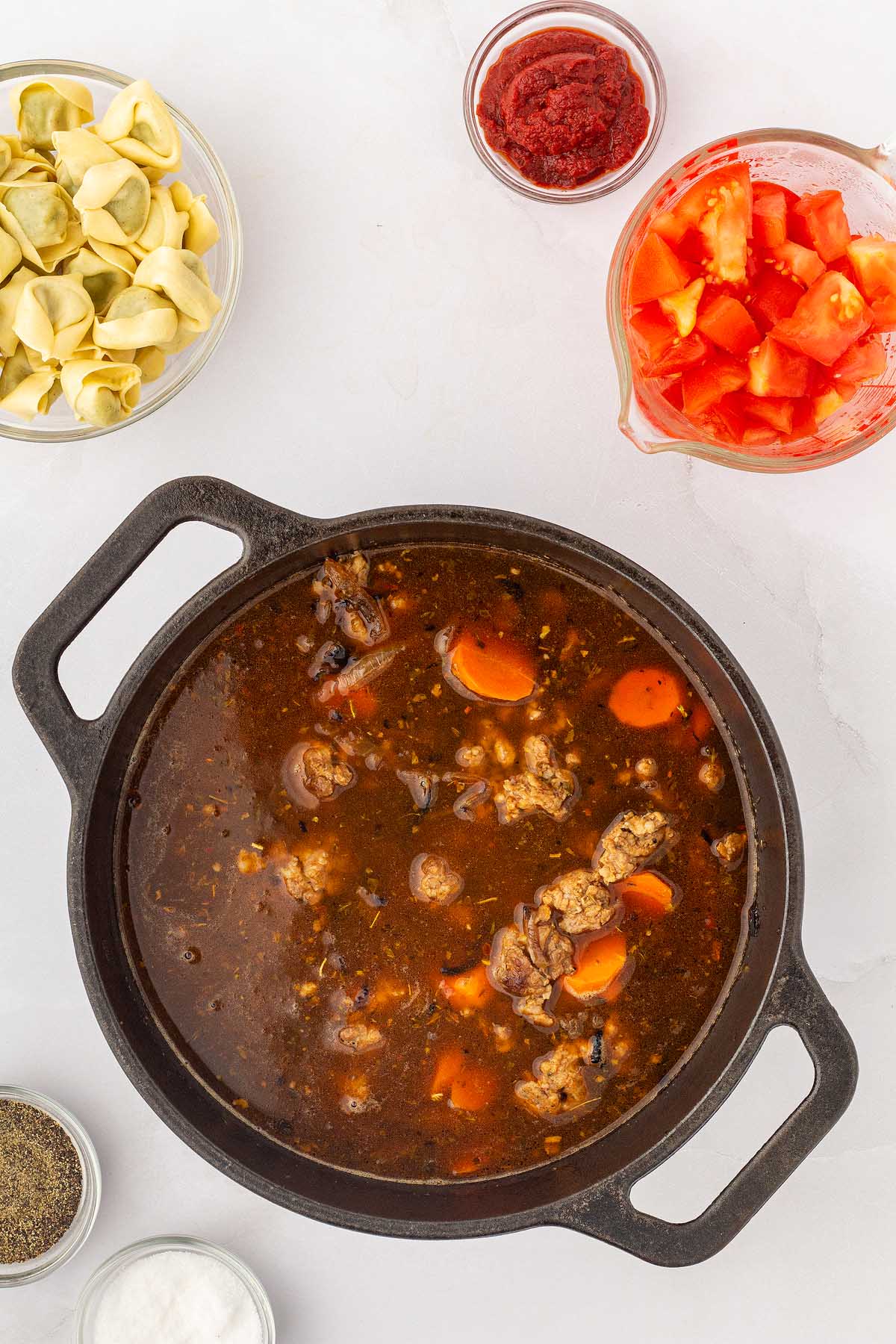 A pot of Italian sausage soup with creamy tortellini on a table.