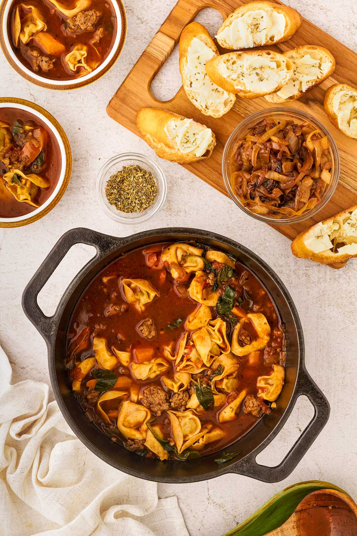 A bowl of creamy sausage tortellini soup and bread on a table.