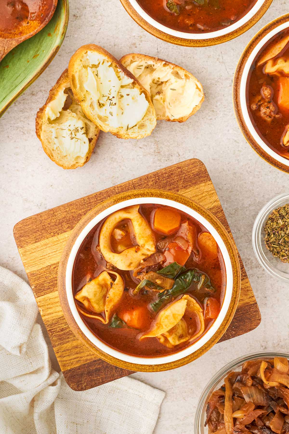 An enticing bowl of creamy sausage tortellini soup, accompanied by a slice of warm bread, is placed delicately on a table.