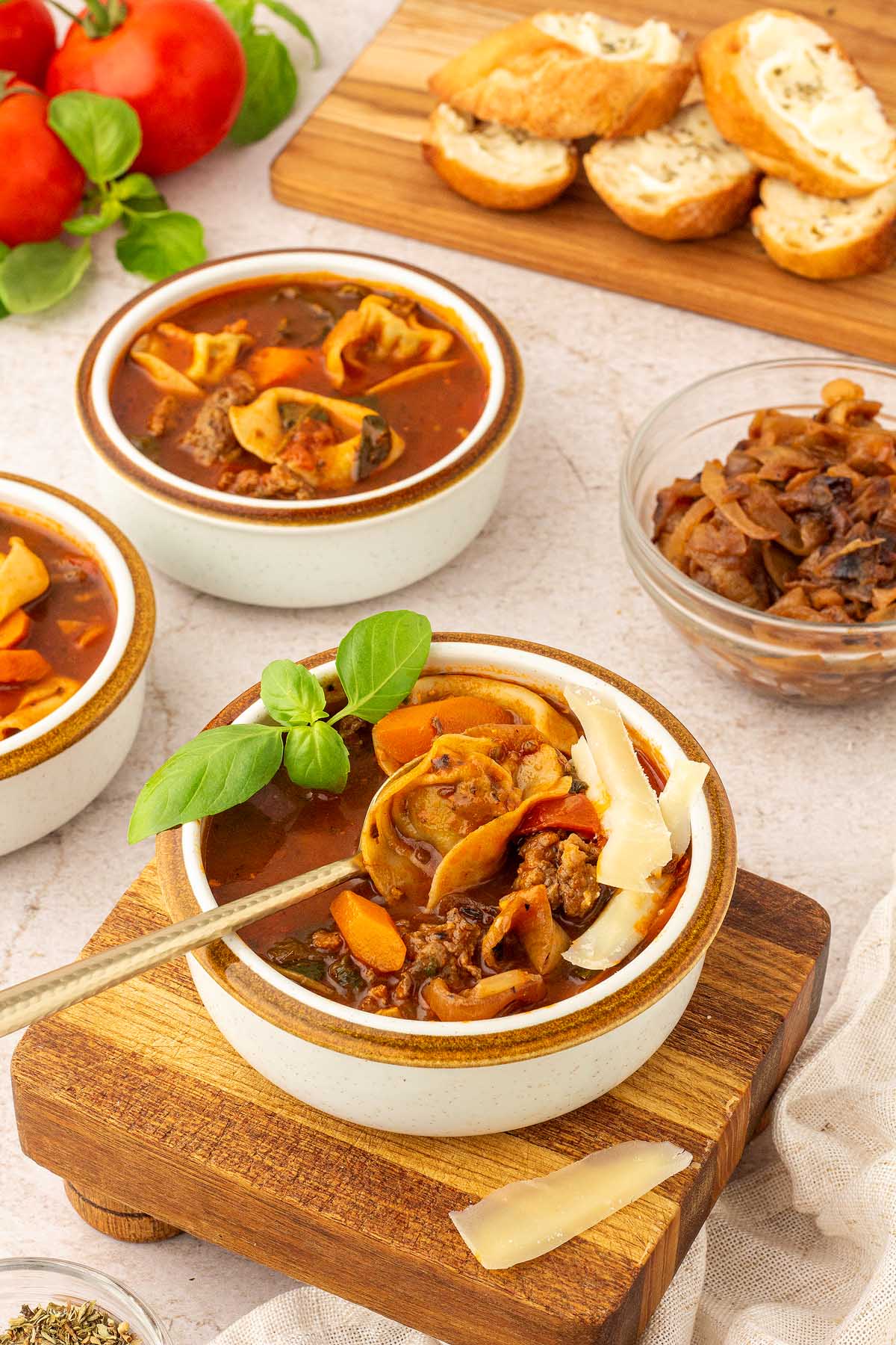 Italian sausage soup with sausage tortellini on a wooden cutting board.