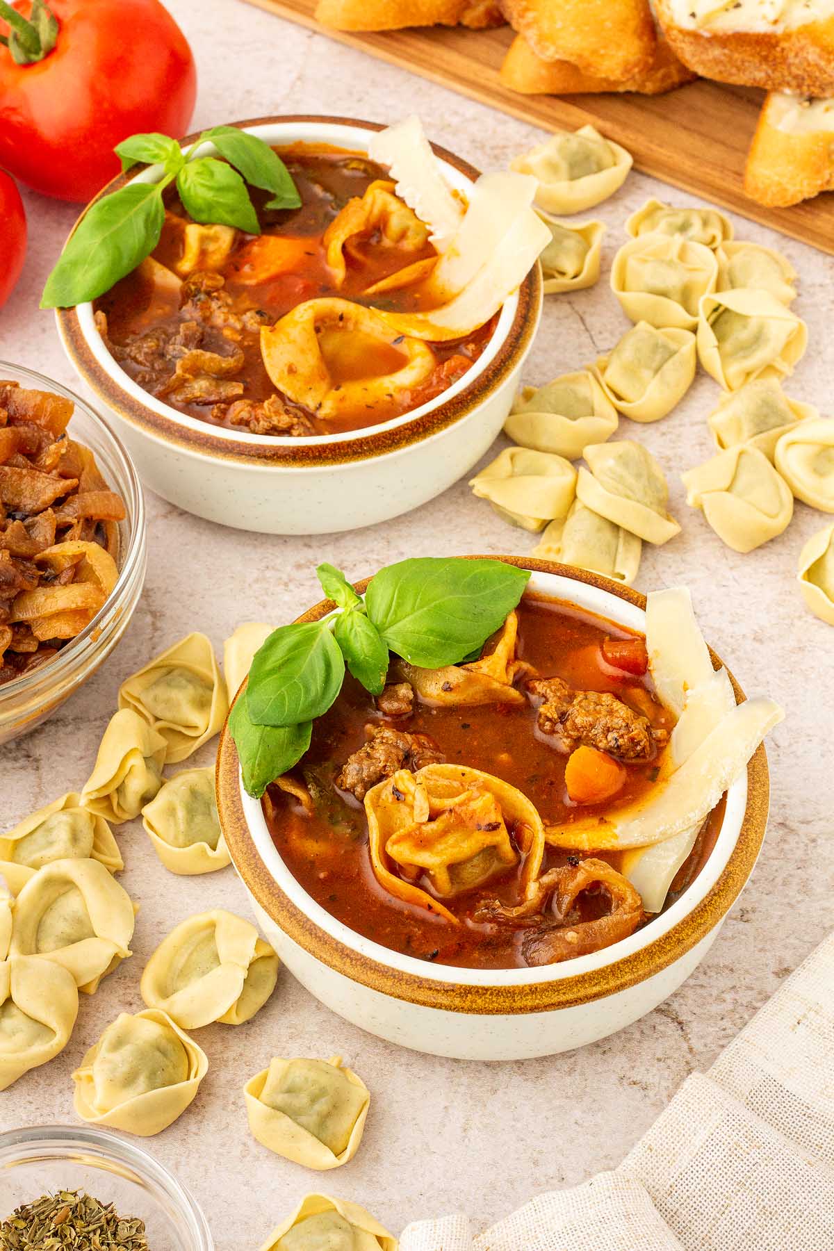 Two bowls of creamy sausage tortellini soup on a table.