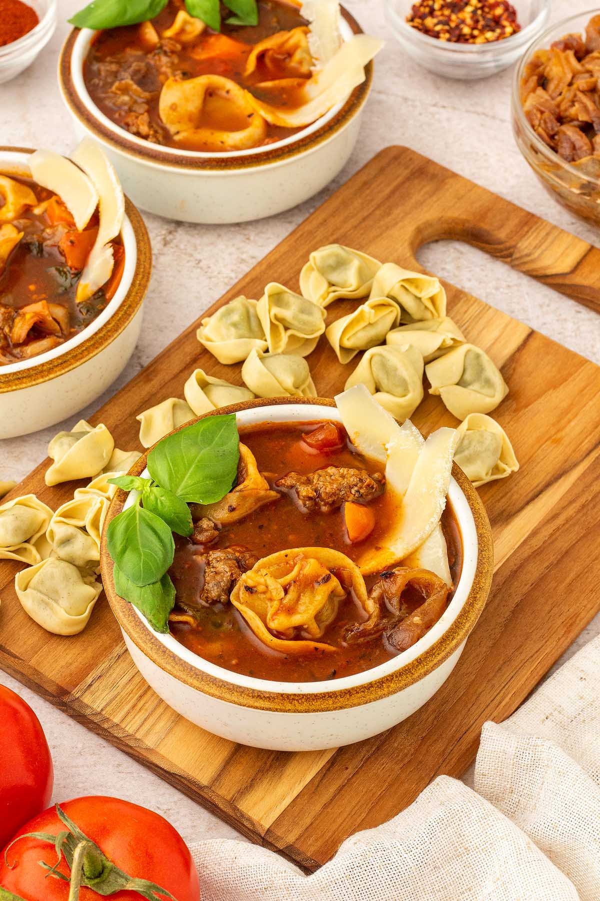 Three bowls of creamy sausage tortellini soup on a cutting board.