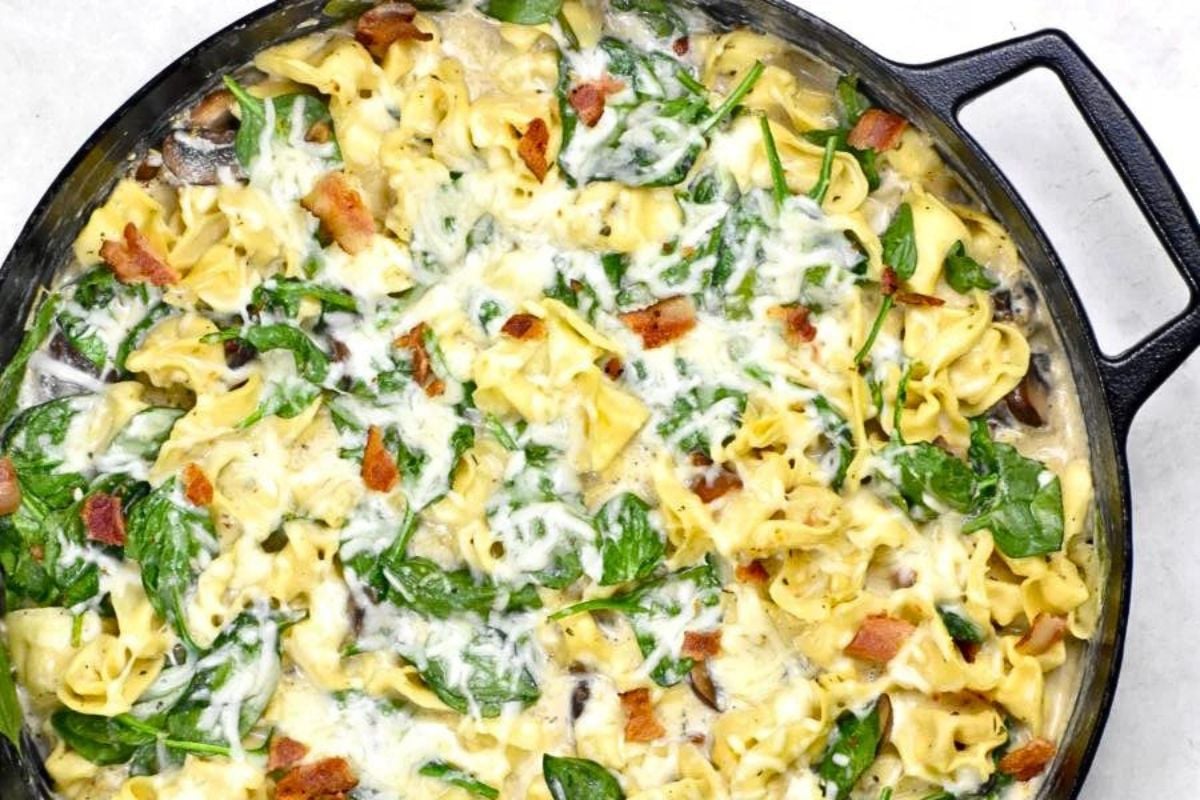 A skillet of tortellini al forno with cream sauce and bacon.