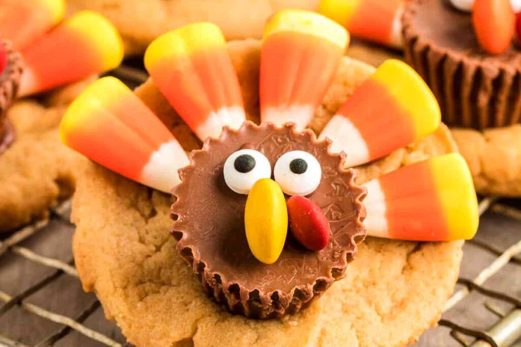 Cookie decorated like a turkey using candy corn, chocolate, and candy eyes on a wire rack—perfect for adding a festive touch to your Friendsgiving celebration.