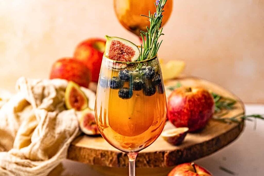 A glass of white wine sangria with fig slices and rosemary.