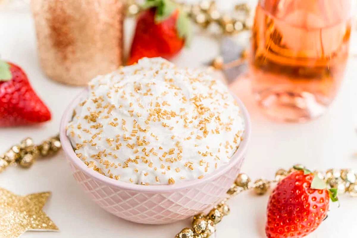 A bowl of whipped dip with gold sprinkles, surrounded by strawberries and festive decorations—perfect for serving as a standout New Year's Eve dessert.