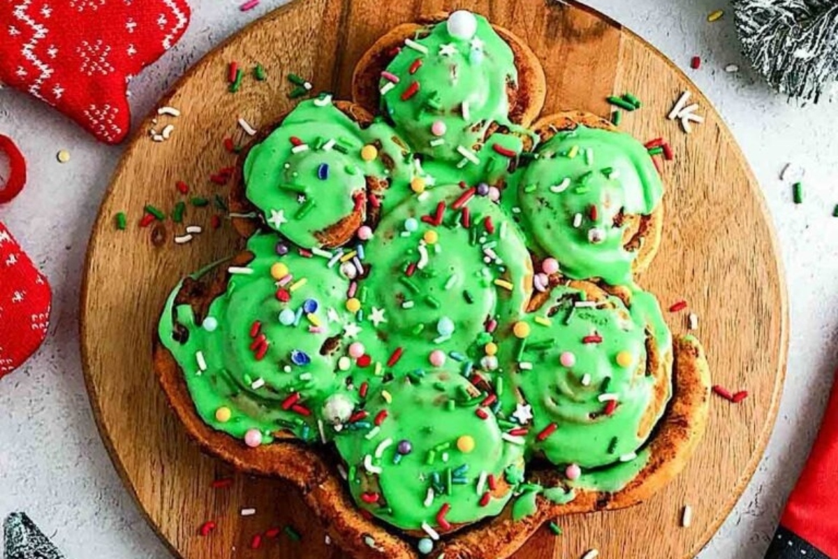 A christmas tree shaped doughnut with green frosting on a wooden cutting board.