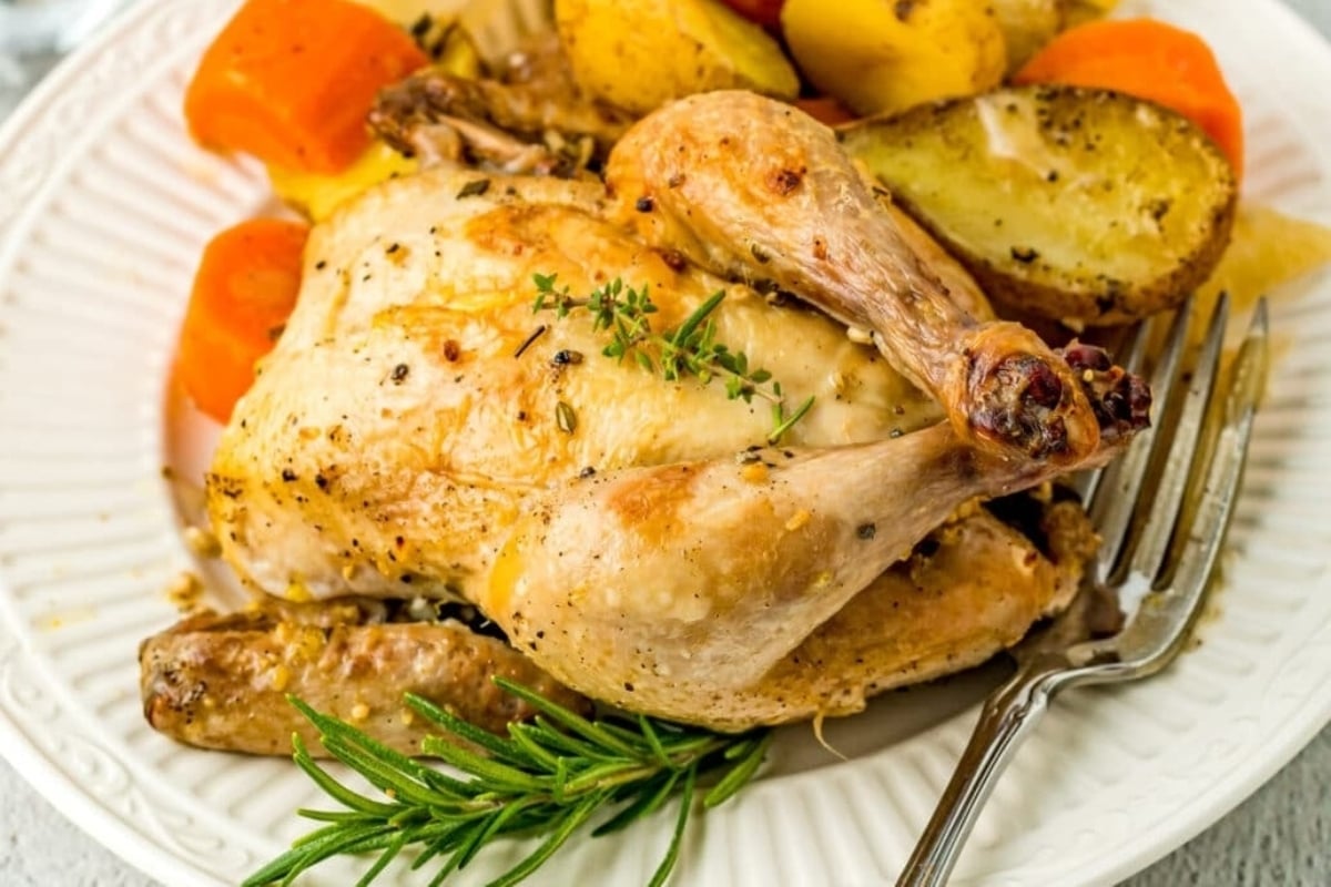 A traditional New Year's dinner featuring succulent roasted chicken served with golden potatoes and tender carrots, elegantly plated on a pristine white dish.