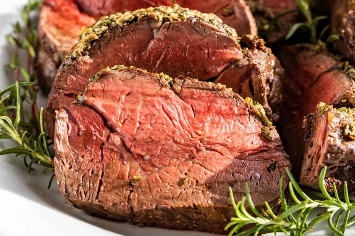 Beef tenderloin with rosemary sprigs, perfect for New Year's dinners, presented on a white plate.