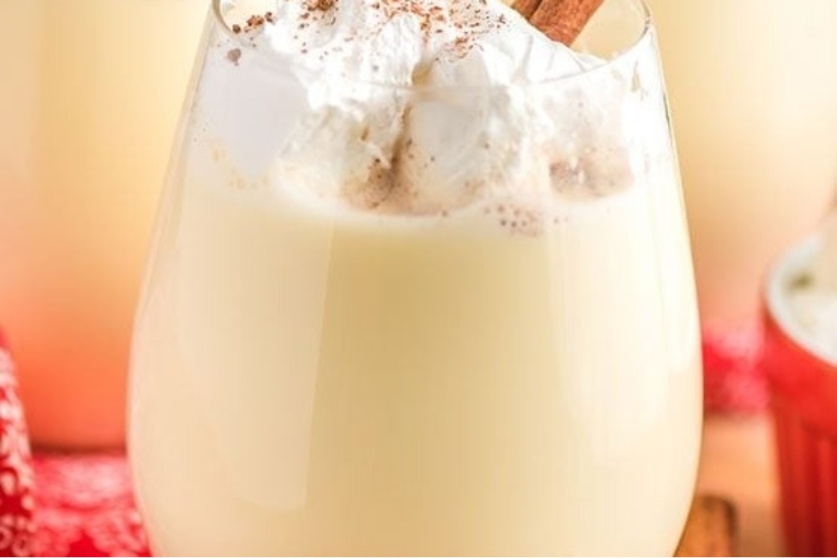 A creamy glass of eggnog topped with a sprinkle of cinnamon and a dollop of whipped cream.