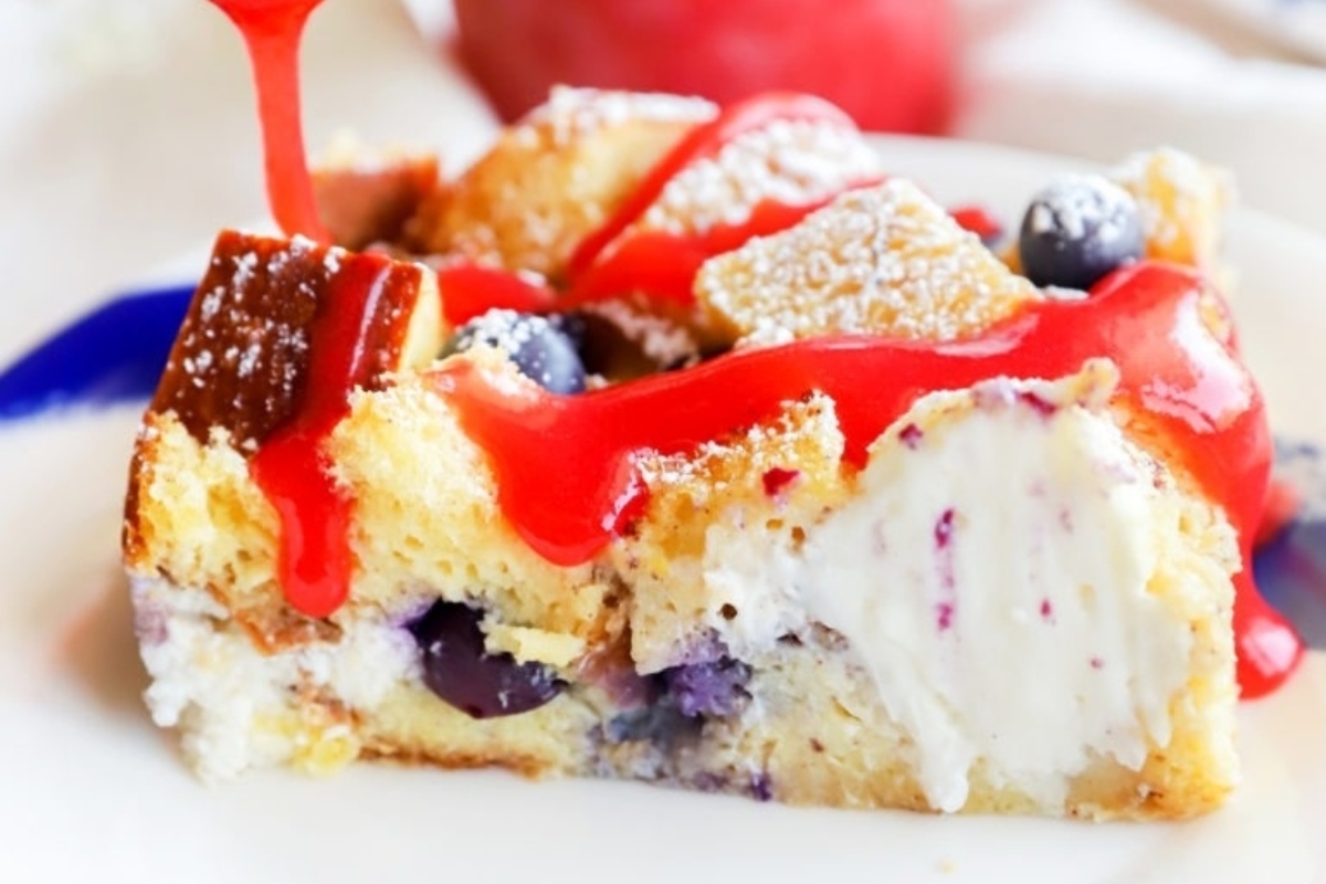 A slice of blueberry bread pudding being drizzled with red sauce, perfect for make ahead holiday dishes.