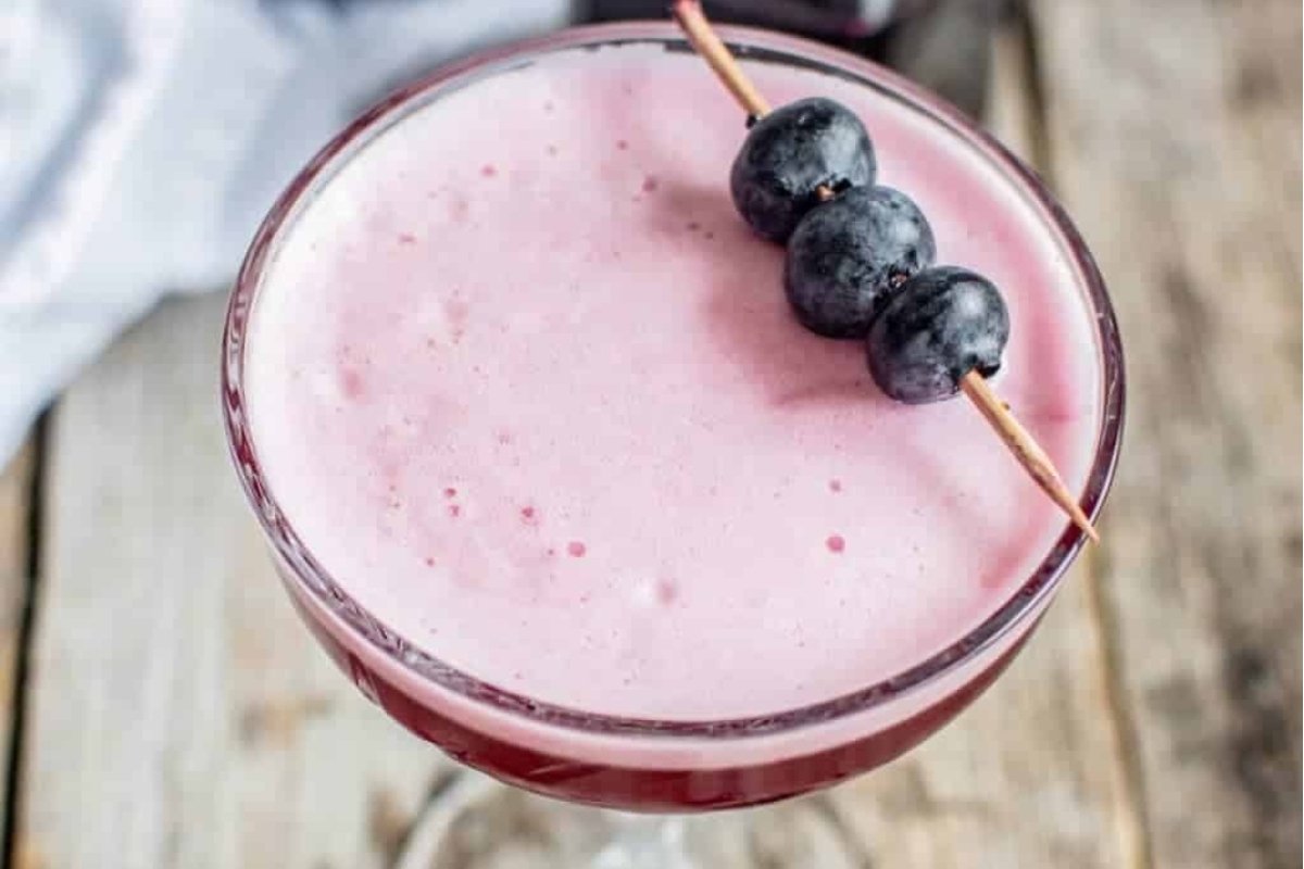 A festive New Year's Eve cocktail featuring a pink drink with plump blueberries adorning the top.