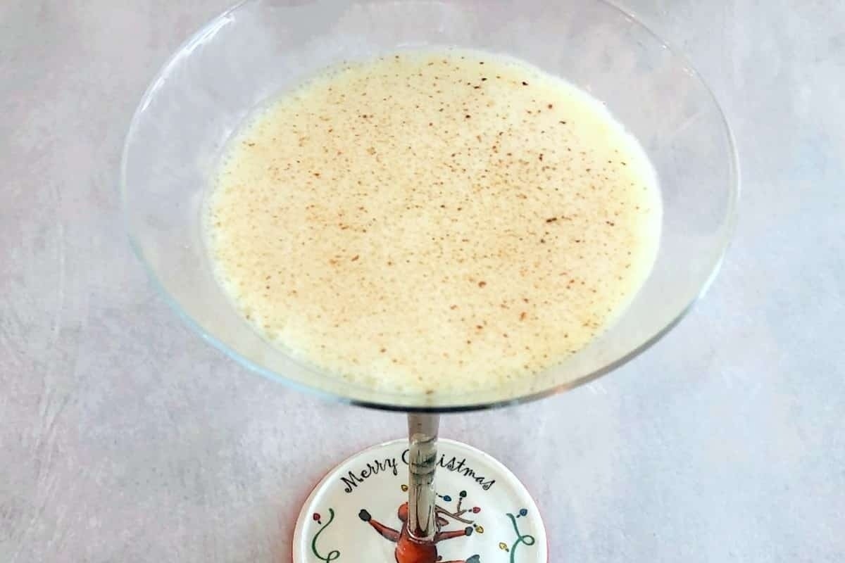 A martini glass containing a festive eggnog cocktail is elegantly displayed on a tabletop.