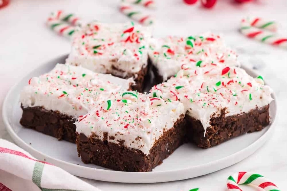 A plate of chocolate brownies topped with whipped cream and garnished with candy canes.