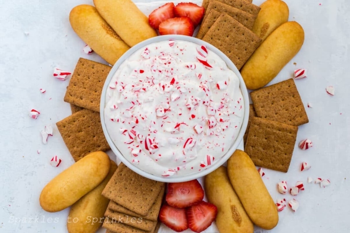 A bowl of peppermint dip with strawberries and crackers, perfect for candy cane lovers.