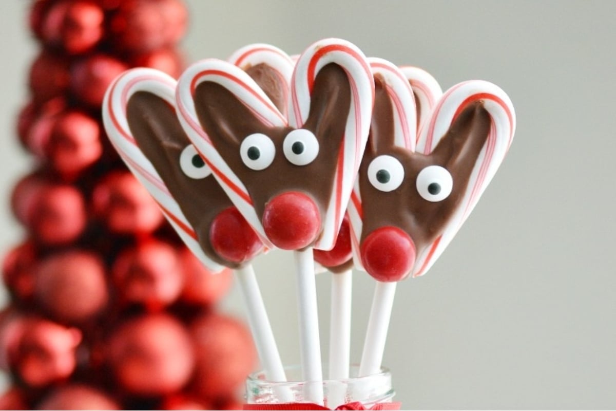 Festive reindeer lollipops displayed in a vase adorned with Christmas decorations.