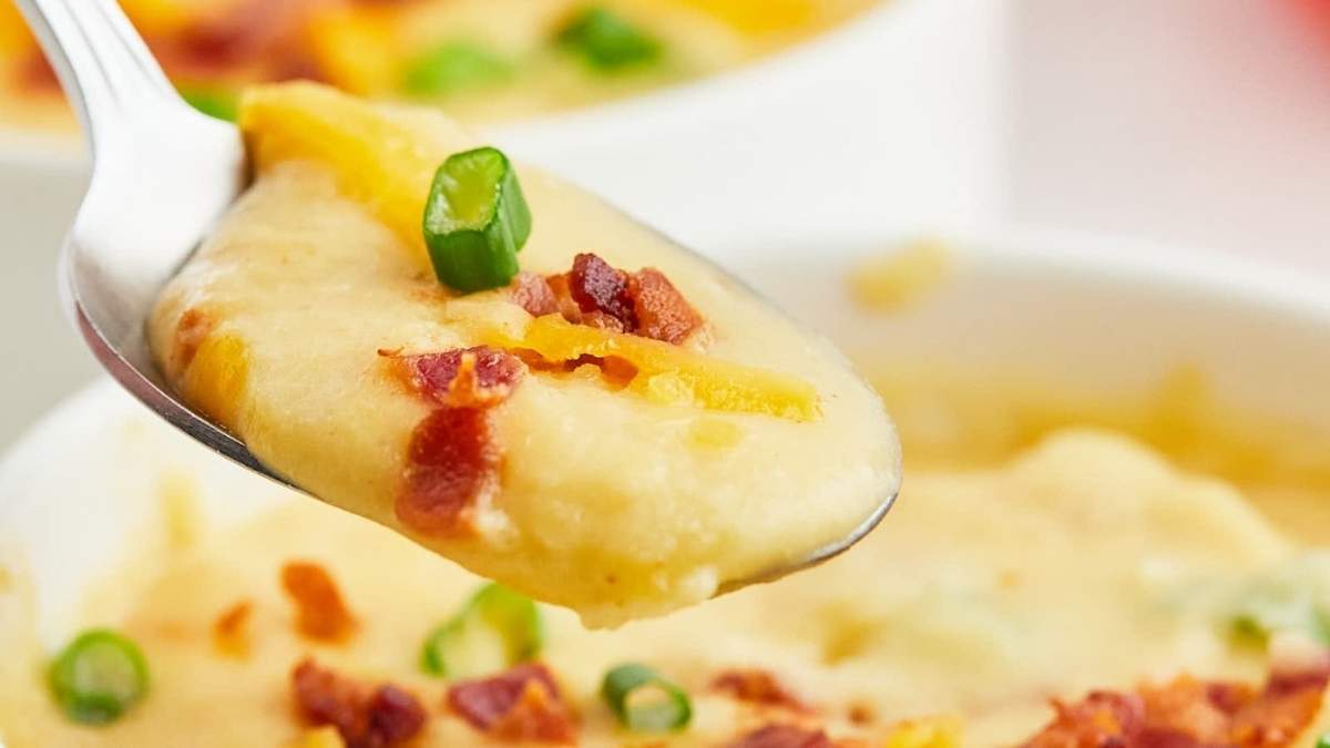 A spoon is holding a bowl of cheesy mashed potatoes.