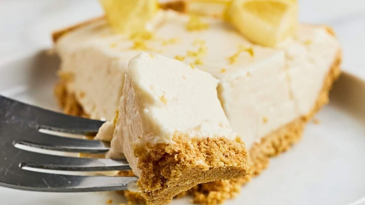 A tangy slice of lemon pie on a plate with a fork.