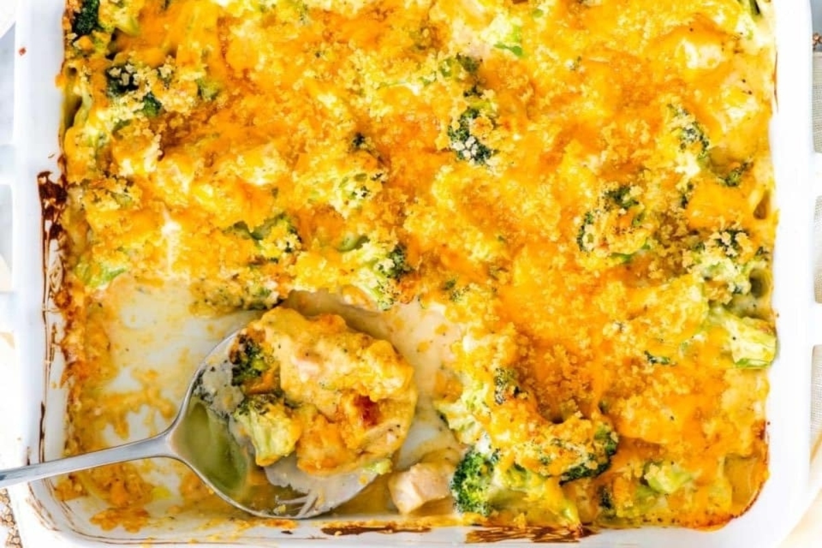 A baking dish of cheesy broccoli casserole with a serving spoon, showing a scoop removed. visible crusty cheese topping and soft texture.