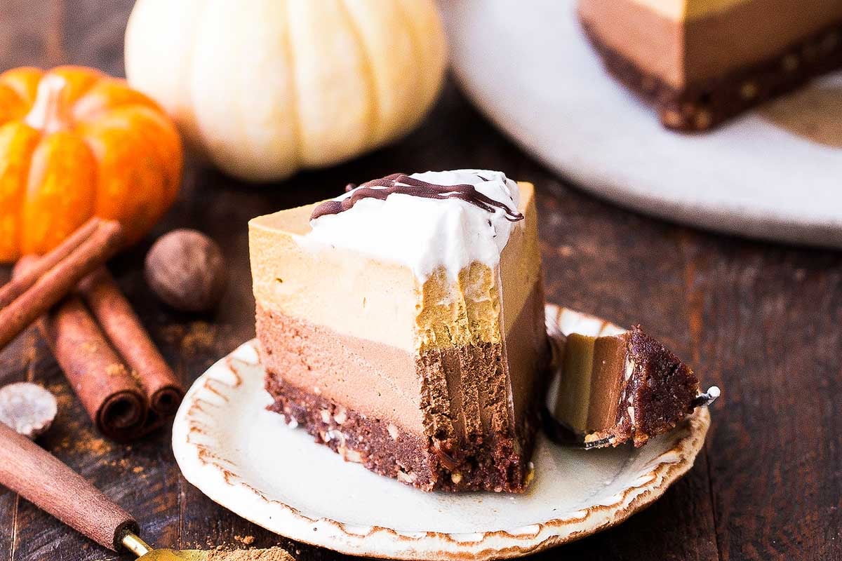 A slice of pumpkin cheesecake on a plate, accompanied by a steaming cup of cocoa.