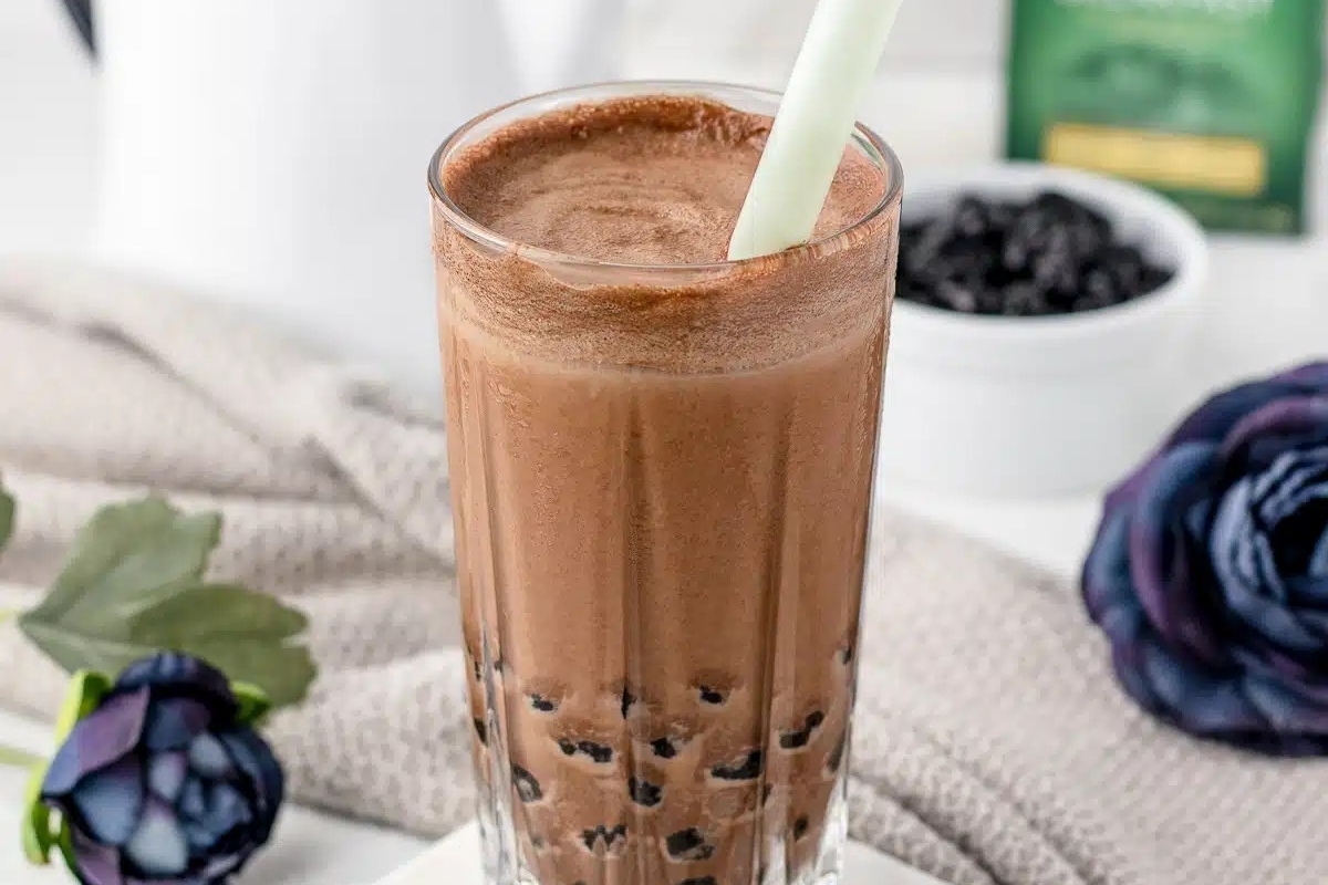 A festive cup of chocolate bubble tea with a green straw.