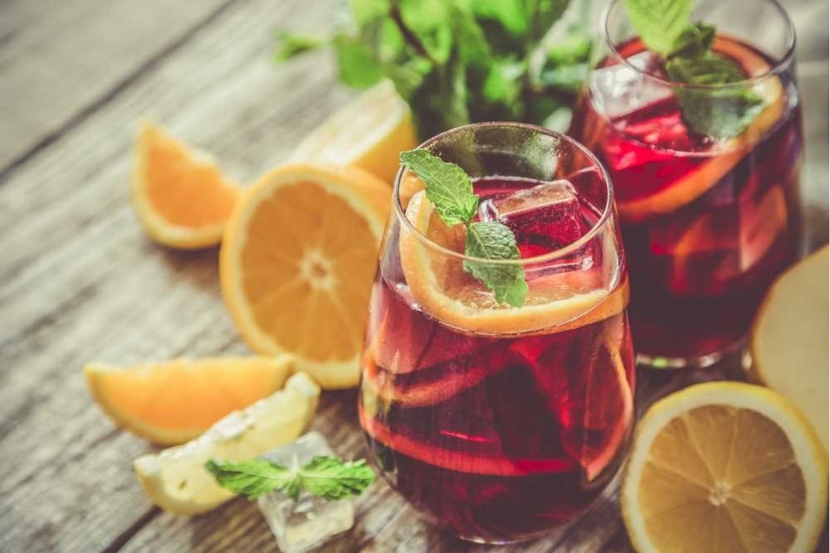 A glass of cranberry sangria with orange slices and mint leaves.